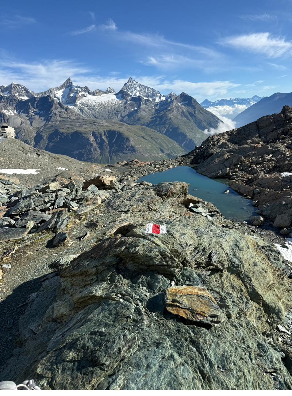 Person auf einem felsigen Alpengipfel mit Wegmarkierung